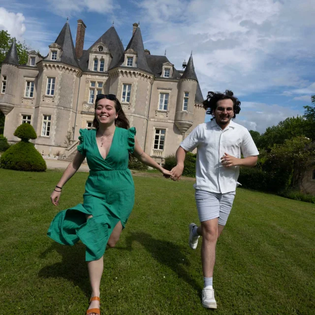 un couple qui se tiennent main dans la main et qui court avec le château de la grange moreau derrière eux